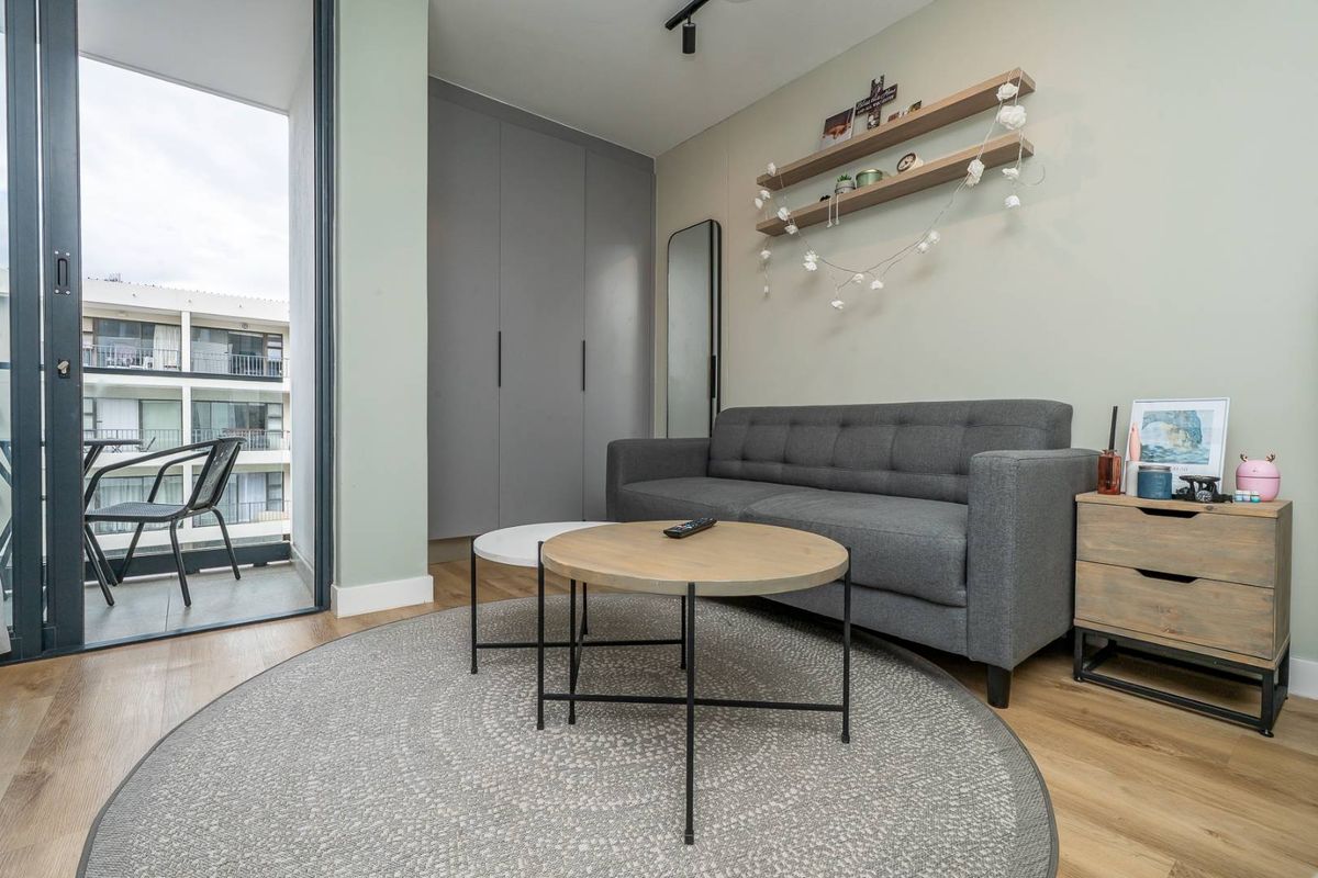 A modern living room featuring light wood flooring, built-in grey cabinetry, and direct access to a private balcony through sliding glass doors.