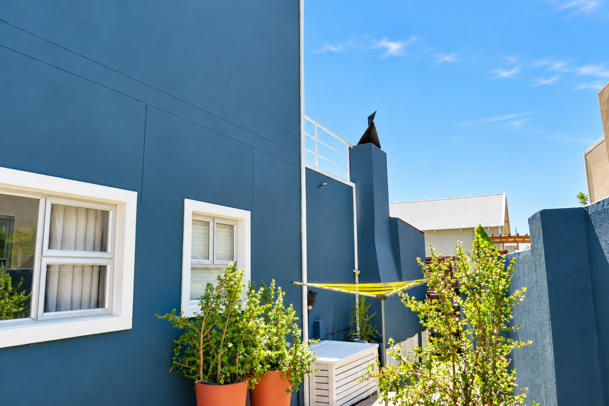 A view of the rear exterior facade featuring a blue painted wall, external chimney, and a paved patio area.