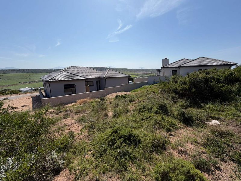 View of the rear elevation of a modern residential property featuring a tiled roof, chimney, and boundary wall, set against a natural landscape.