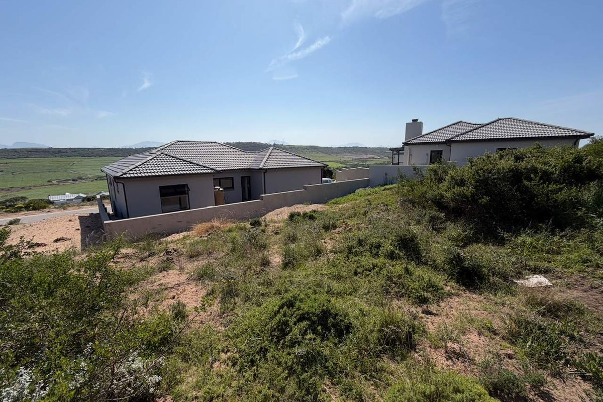 View of the rear elevation of a modern residential property featuring a tiled roof, chimney, and boundary wall, set against a natural landscape.