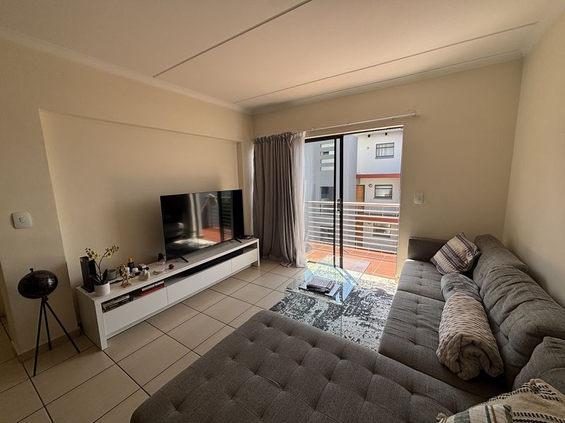 A bright living room featuring tiled flooring and a sliding glass door that opens onto a private balcony.