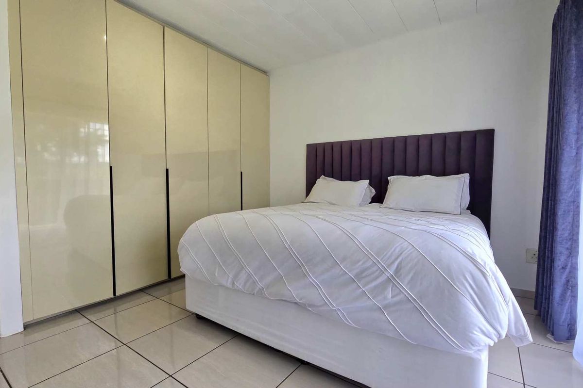 A well-maintained bedroom featuring large, high-gloss built-in cupboards and neutral tiled flooring, providing ample storage space.