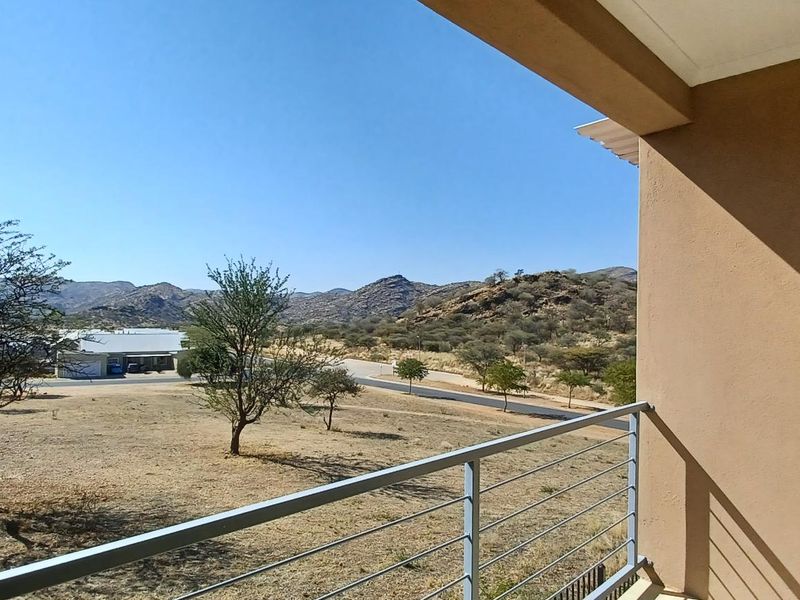 A covered balcony featuring a metal railing and an exterior wall light, offering expansive views of the surrounding landscape.