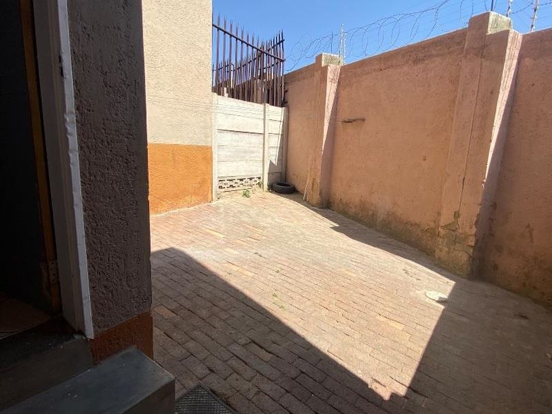 A private rear courtyard featuring brick paving, enclosed by high perimeter walls with security razor wire and concrete steps leading to the dwelling.