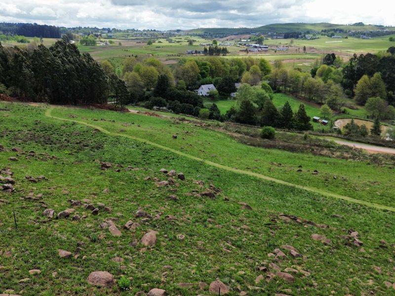 An aerial view of a large, sloped vacant residential plot featuring natural vegetation and rocky terrain with expansive countryside views.
