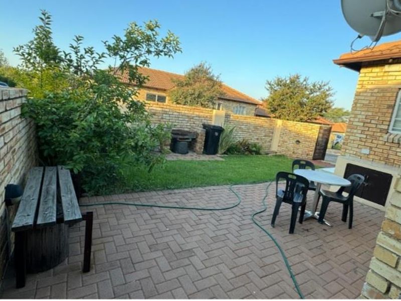 A private rear courtyard featuring a paved patio area, a built-in braai, and a small lawn enclosed by brick boundary walls.