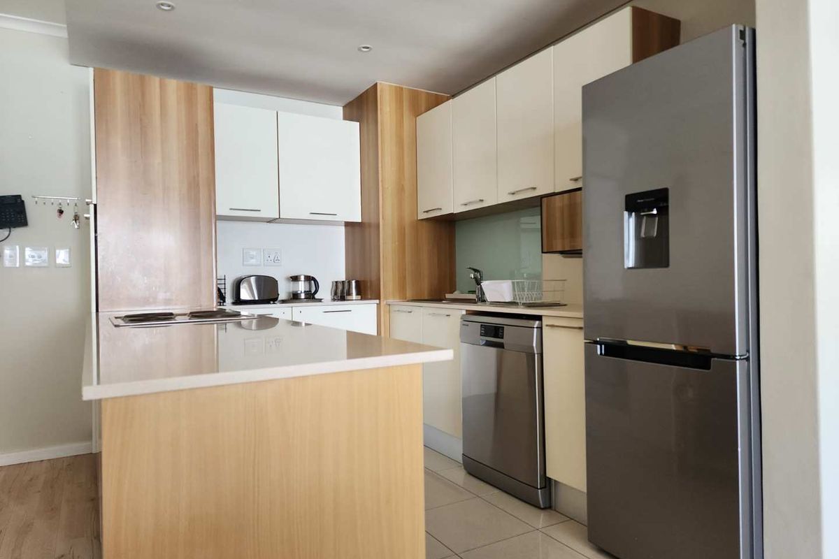 Modern kitchen featuring light wood and white cabinetry, stone countertops, integrated hob, and stainless steel appliances, including a dishwasher and refrigerator.