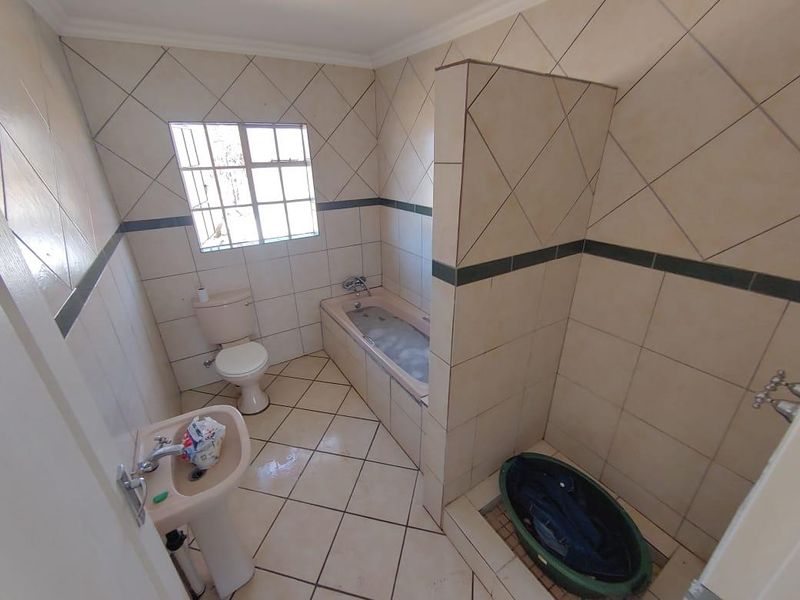 A functional bathroom featuring a built-in bathtub, separate shower area, pedestal basin, and toilet with neutral wall and floor tiling.