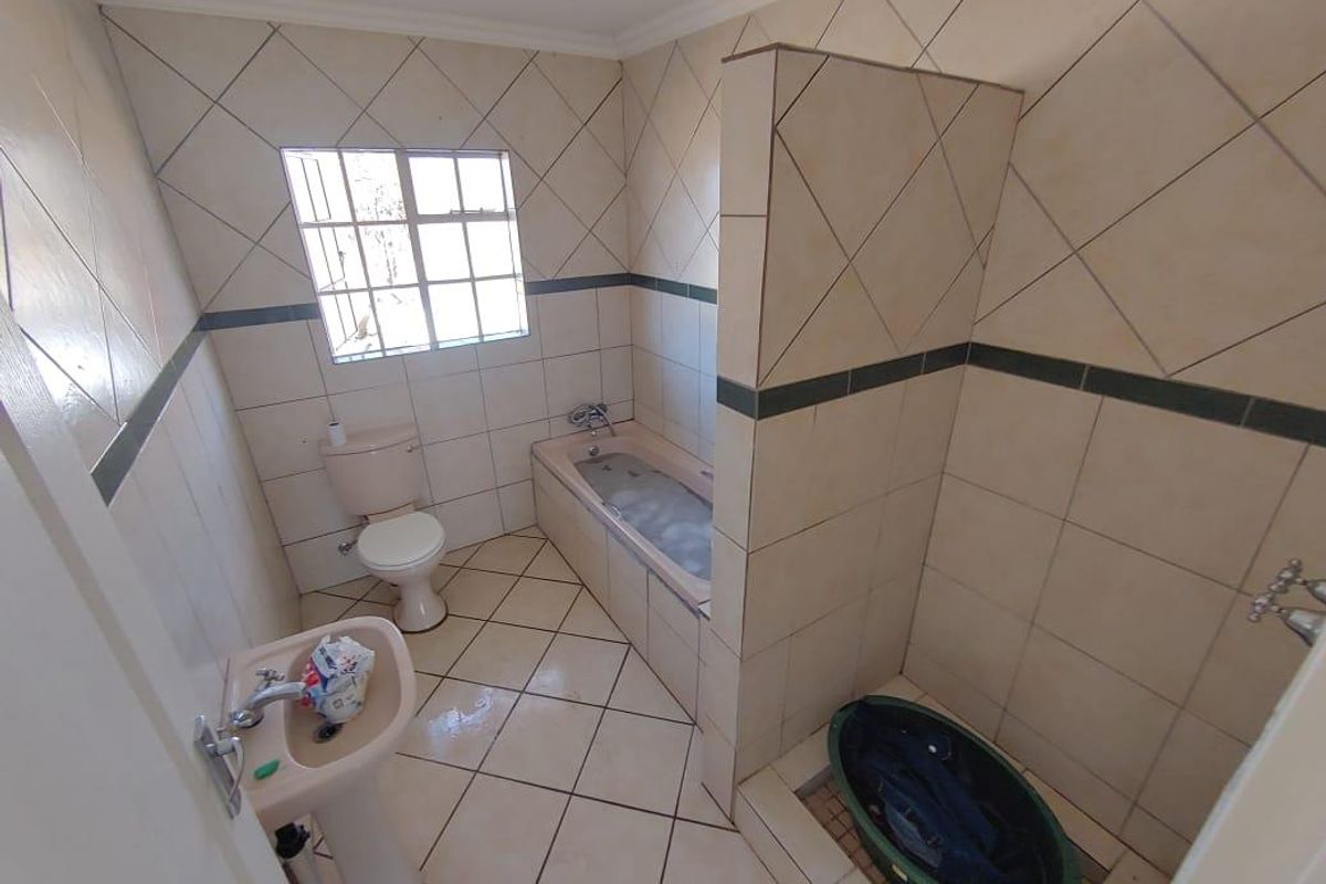 A functional bathroom featuring a built-in bathtub, separate shower area, pedestal basin, and toilet with neutral wall and floor tiling.