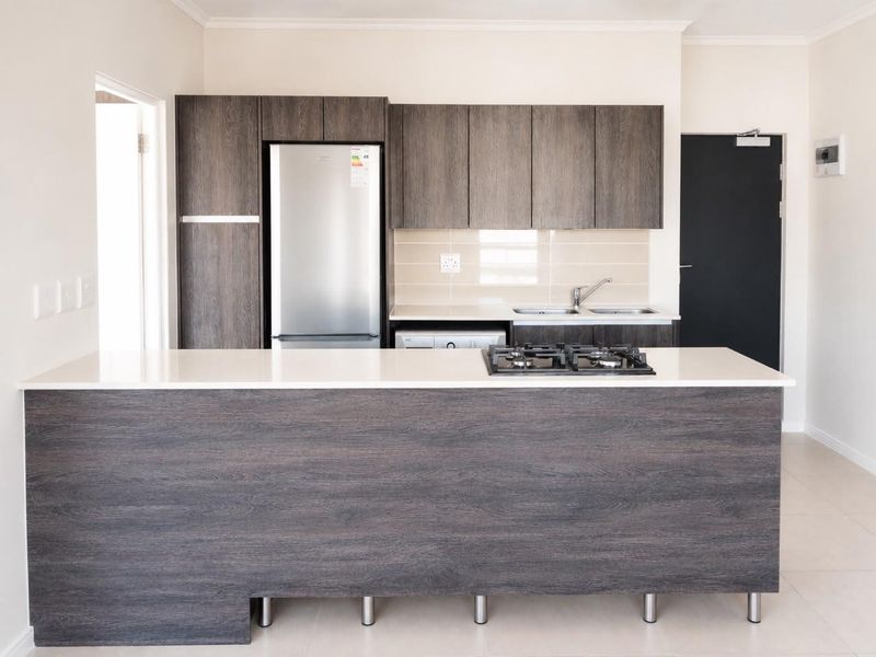 Modern kitchen featuring dark wood-grain cabinetry, stone countertops, a built-in gas hob, and a stainless steel sink with a tiled backsplash.