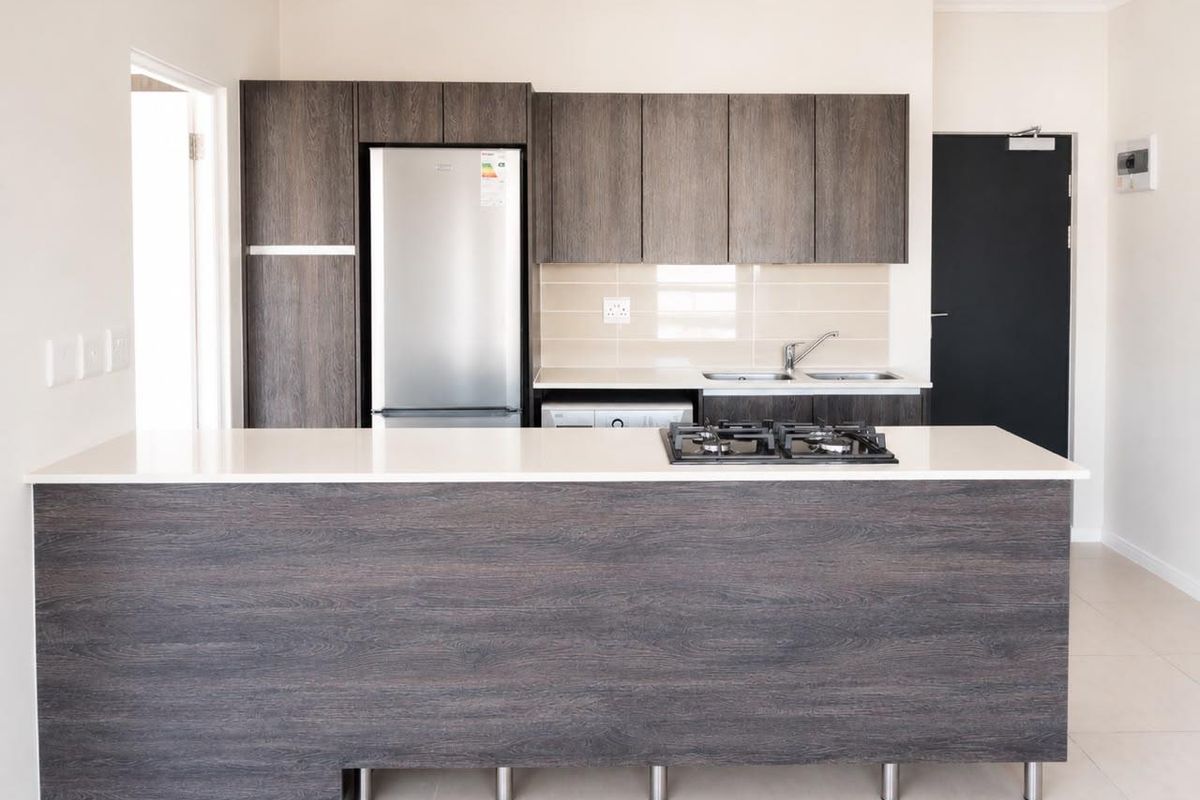 Modern kitchen featuring dark wood-grain cabinetry, stone countertops, a built-in gas hob, and a stainless steel sink with a tiled backsplash.