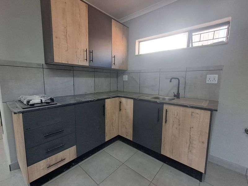 Modern kitchen featuring two-tone cabinetry, laminate countertops, a stainless steel sink with a black mixer tap, and a built-in gas hob.
