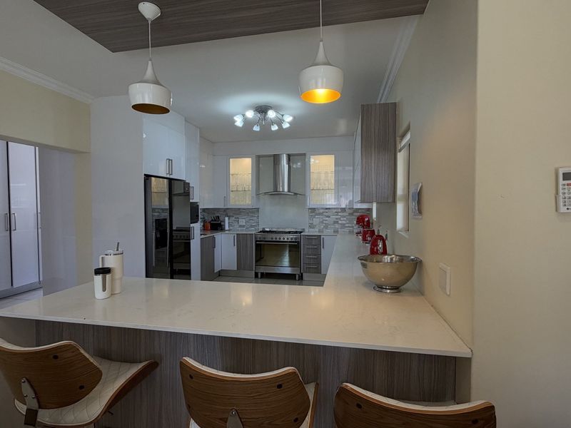 Modern kitchen featuring sleek cabinetry, stone countertops, a breakfast bar, and integrated stainless steel appliances, complemented by stylish pendant lighting.