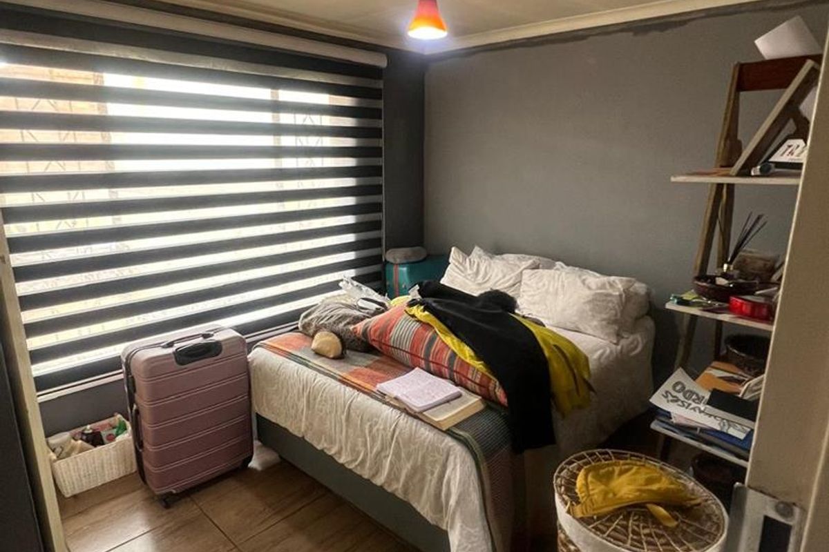 A compact bedroom featuring tiled flooring, a large window with fitted blinds, and a neutral grey accent wall.