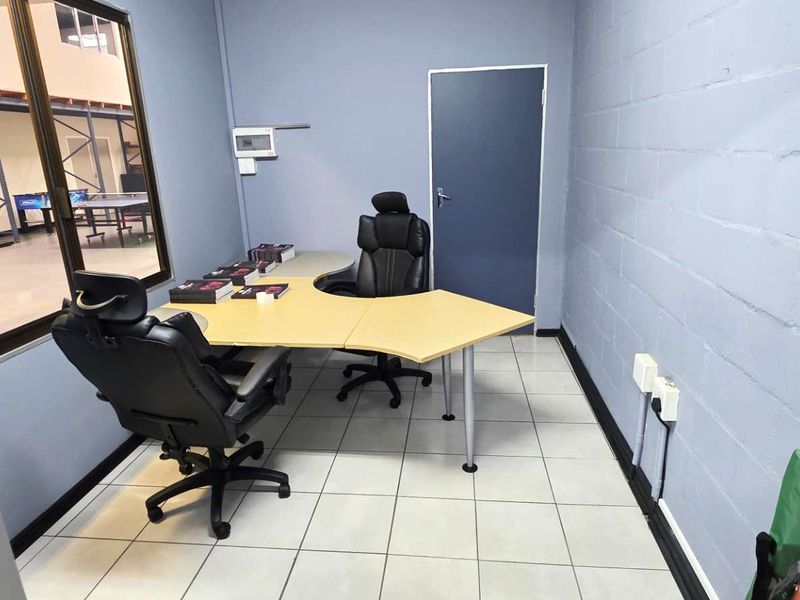 A functional office space featuring tiled flooring, painted blockwork walls, and an internal window overlooking the warehouse area.