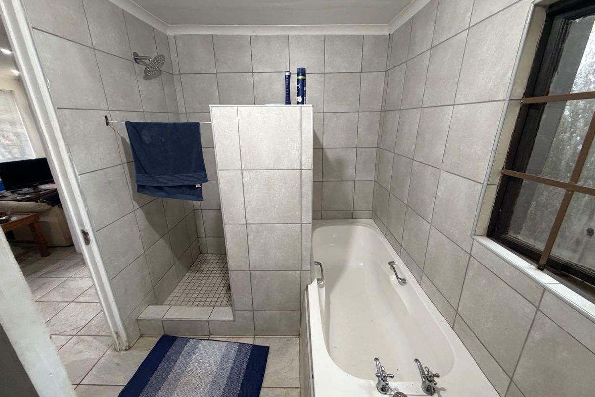 A functional bathroom featuring a combined walk-in shower and built-in bathtub with neutral wall and floor tiling.