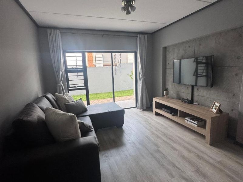 Modern living room featuring laminate flooring, a concrete accent wall, and a sliding glass door providing access to the outdoor area.