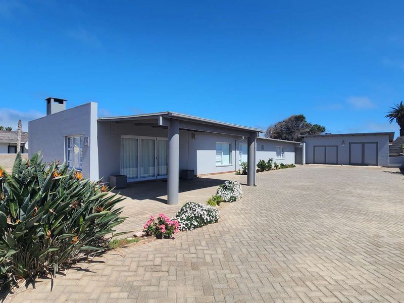 A well-maintained single-story house featuring a spacious paved driveway, a covered patio area, and a detached garage, set within a secure boundary wall.
