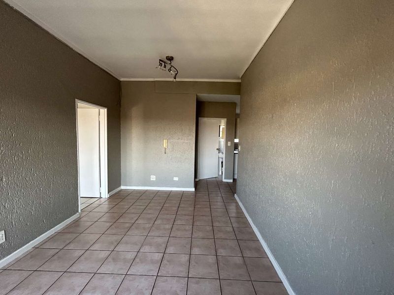 An empty living area featuring neutral textured walls and tiled flooring, providing a blank canvas for interior design and furniture placement.