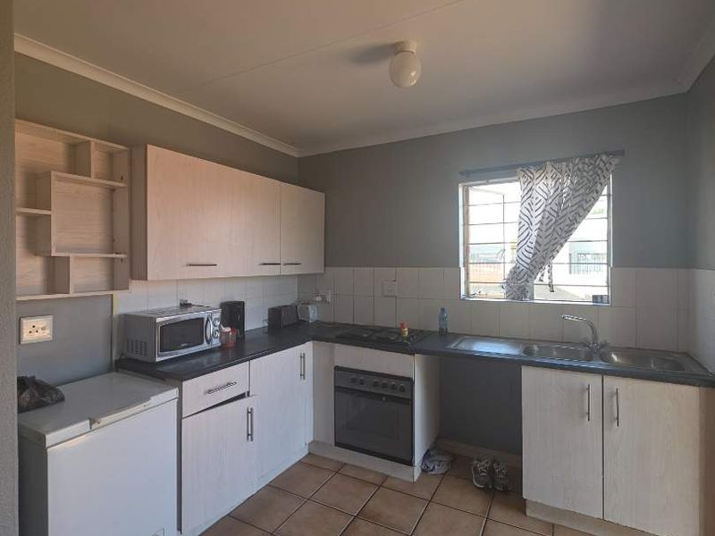 Functional kitchen featuring built-in cabinetry, laminate countertops, integrated oven and hob, double sink, and tiled flooring with a neutral backsplash.