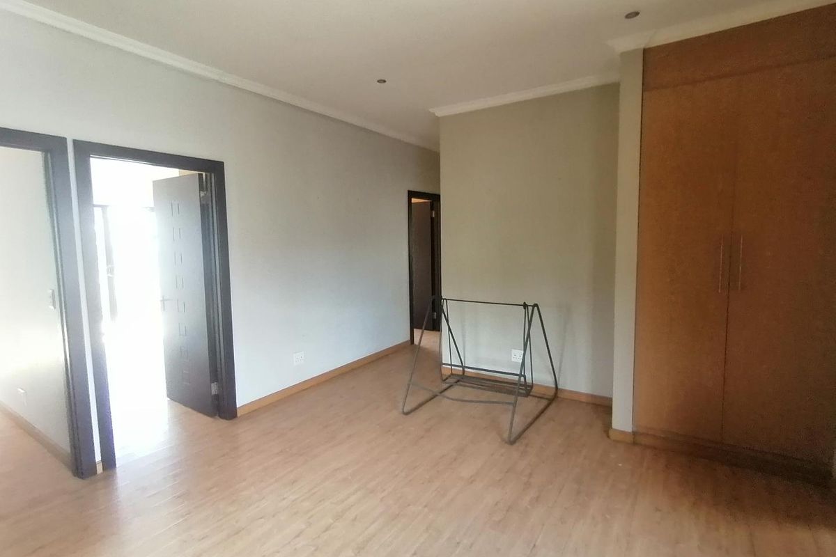 A spacious, empty bedroom featuring light-toned laminate flooring, built-in wooden cupboards, and recessed ceiling lighting.