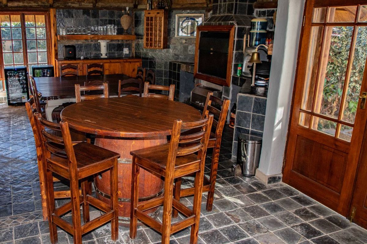 Rustic entertainment area featuring a built-in braai, slate tile flooring, and a traditional thatched roof, offering a cozy atmosphere for social gatherings.