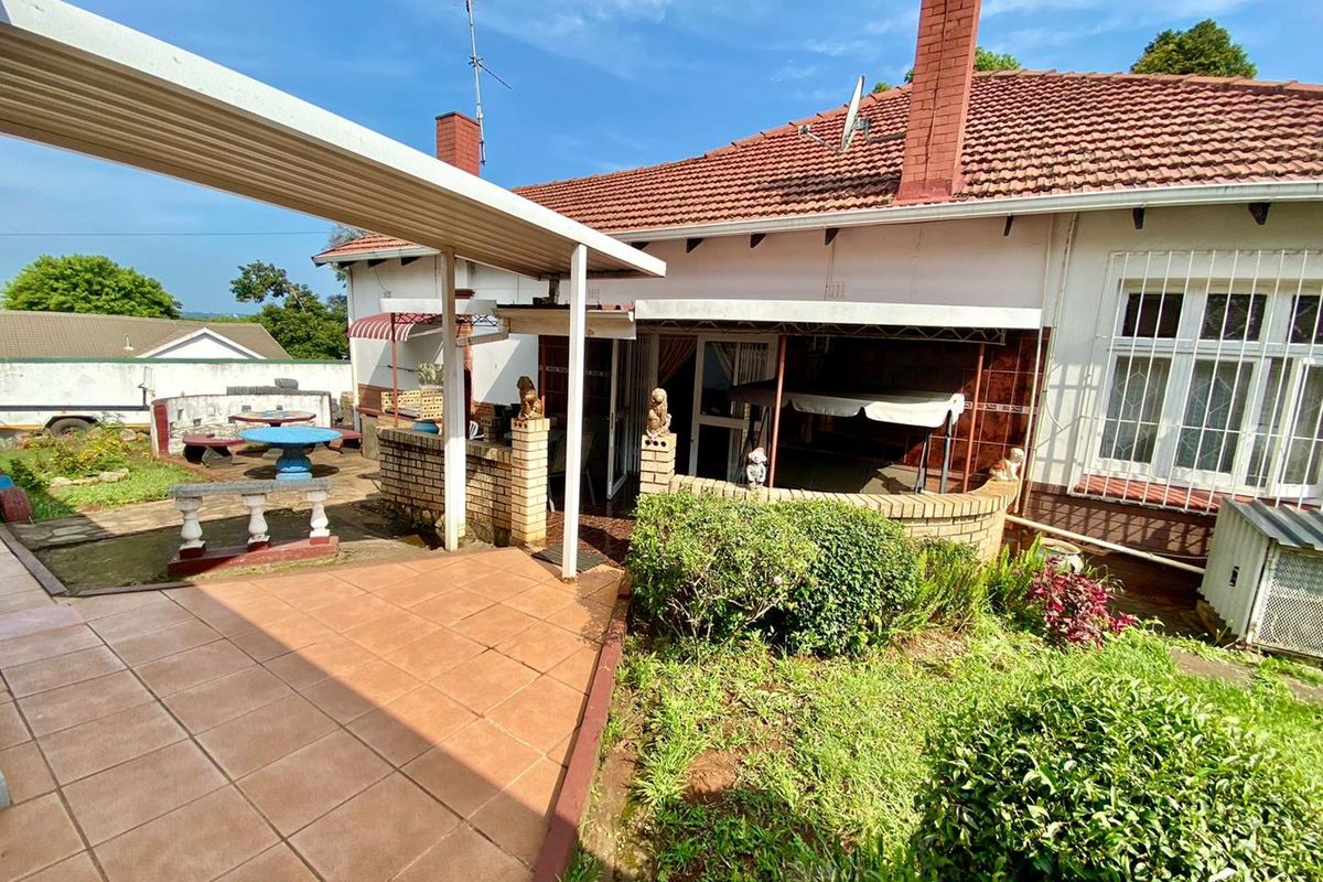 Rear exterior view of the house featuring a covered tiled patio, brick chimney, and garden area with established landscaping.