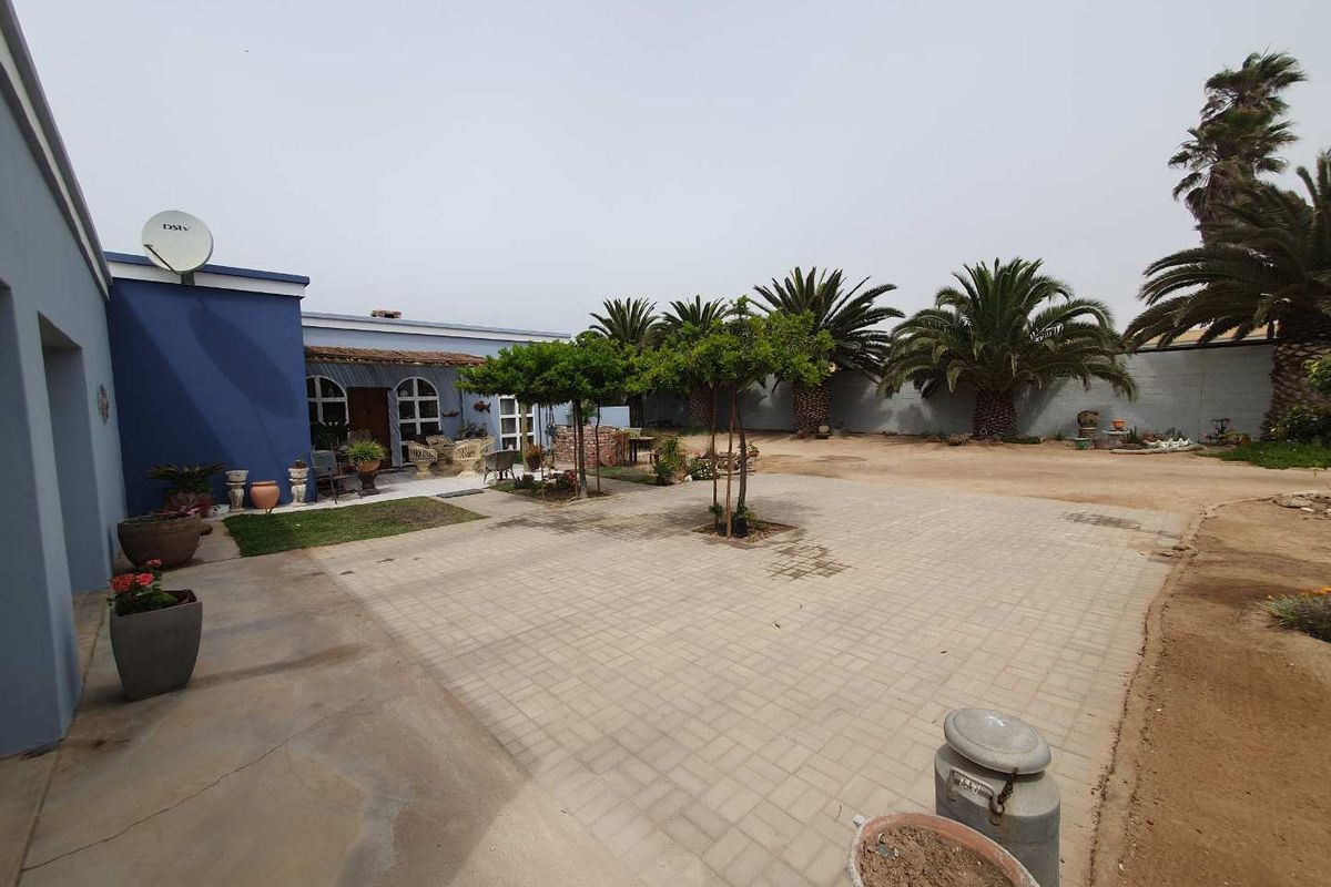 Spacious rear courtyard featuring paved areas, established trees, and a blue-painted exterior wall, providing a functional outdoor space for relaxation and entertainment.