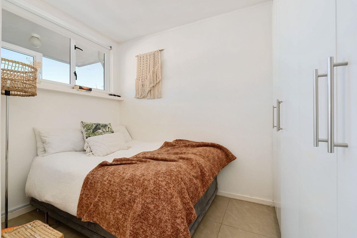 A compact bedroom featuring tiled flooring, a built-in wardrobe, and a sliding window providing natural light.