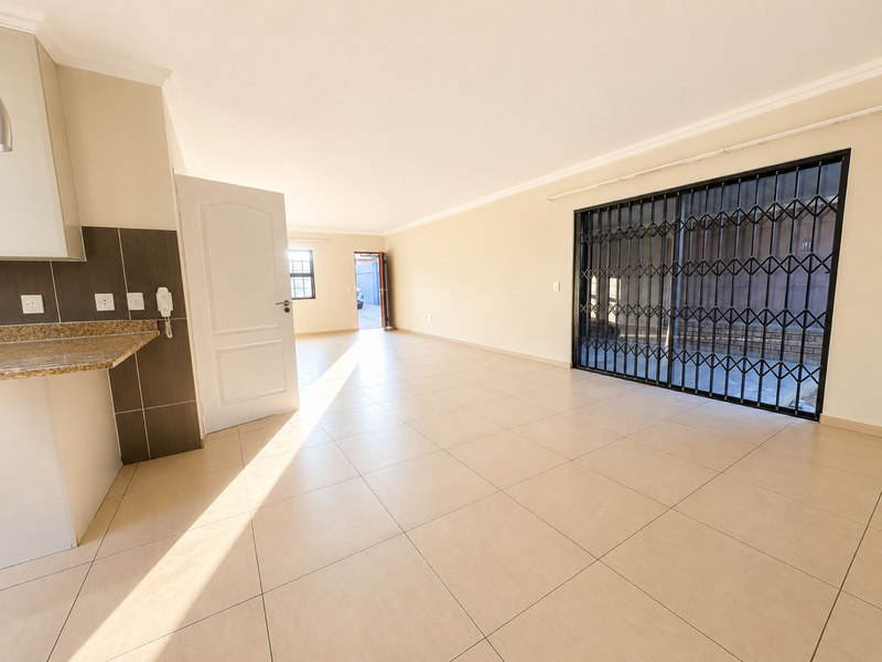 Spacious open-plan living area featuring neutral tiled flooring, granite kitchen counter, and a large sliding door with a security gate leading outdoors.