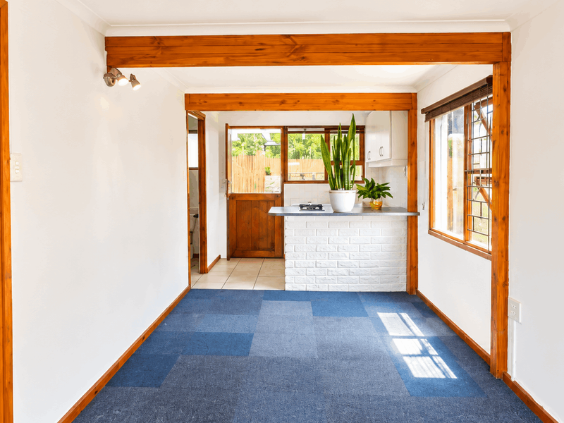 An open-plan living and kitchen area featuring exposed timber beams, a brick breakfast bar, and direct access to the rear exterior.