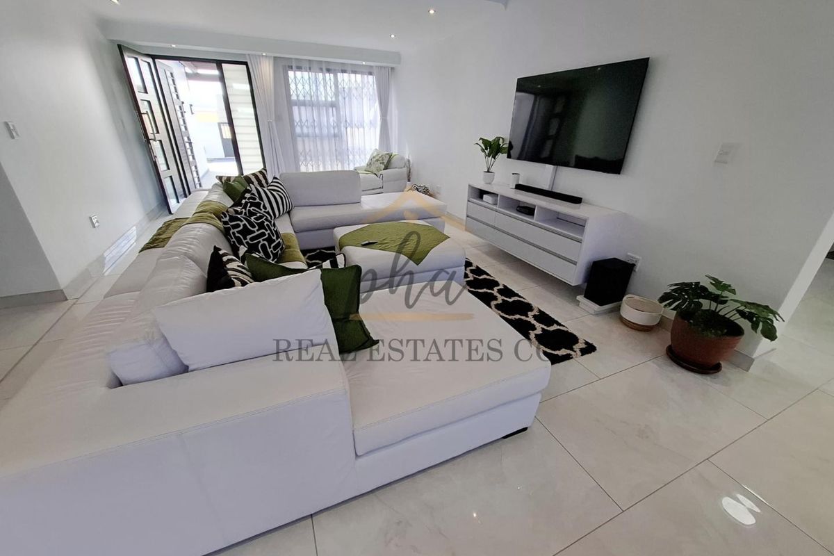 A bright and modern living room featuring large format floor tiles, recessed downlighting, and sliding glass doors leading to an outdoor area.
