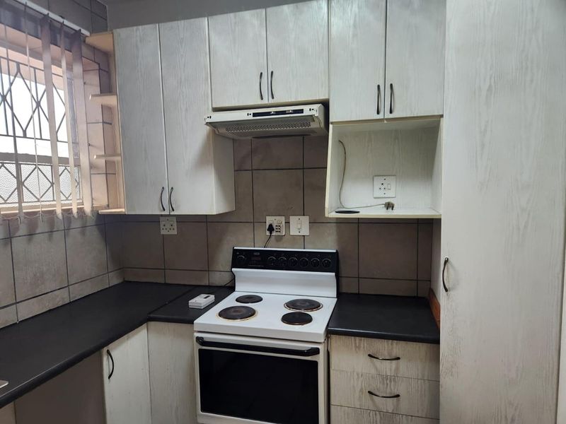A functional kitchen featuring built-in cabinetry, laminate countertops, a tiled backsplash, and a freestanding electric stove with an integrated extractor fan.