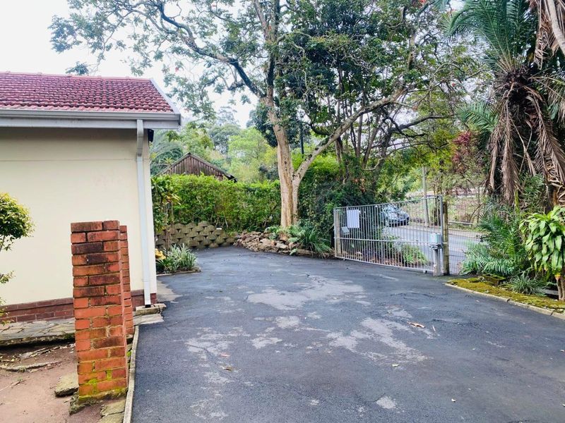 A view of the property entrance featuring an asphalt driveway, brick pillar, and metal security gate leading to the street.