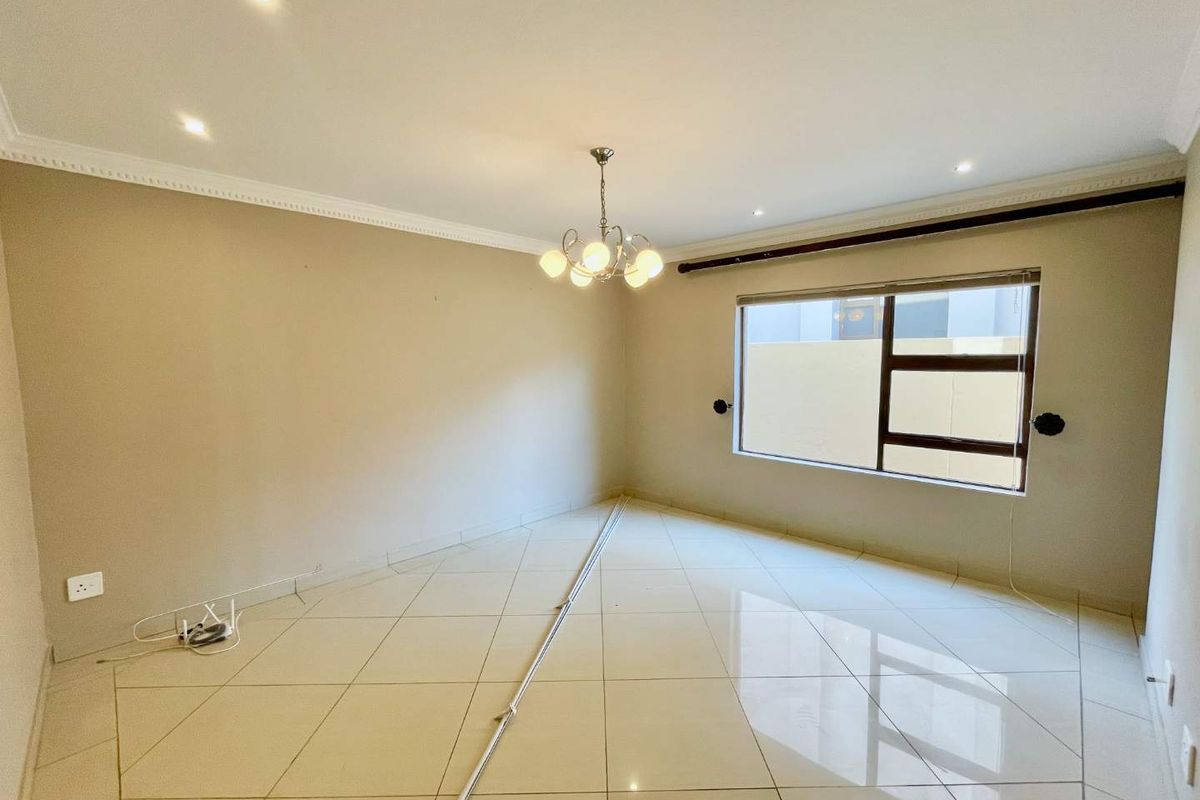 A bright, empty living room featuring polished tiled flooring, decorative cornicing, and a central chandelier, offering a clean canvas for interior design.