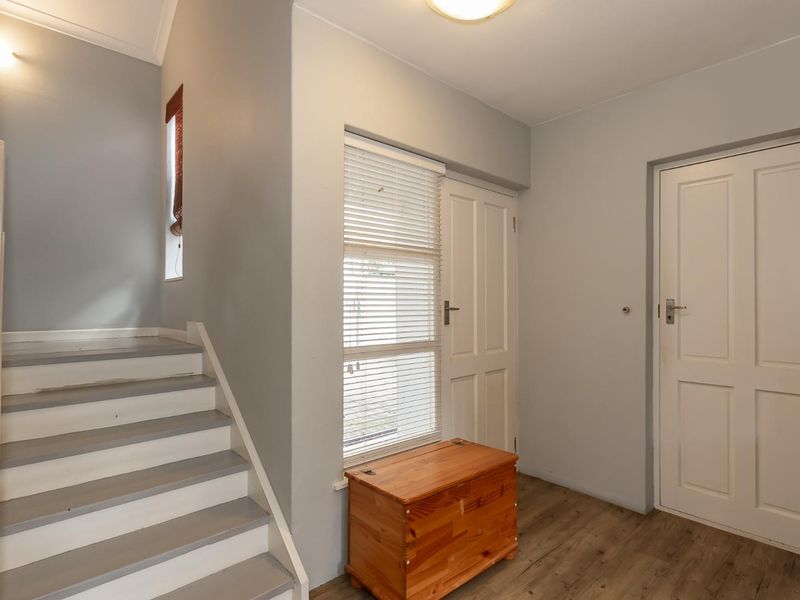 A bright and welcoming entrance hall featuring a staircase, neutral wall tones, timber-look flooring, and panelled interior doors.
