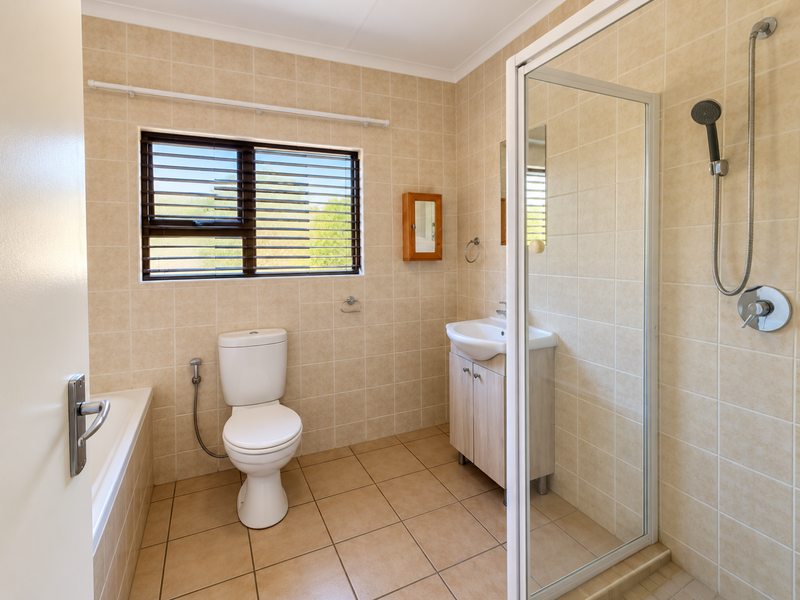 A clean, functional bathroom featuring a separate shower enclosure, bathtub, vanity basin, and neutral wall and floor tiling.