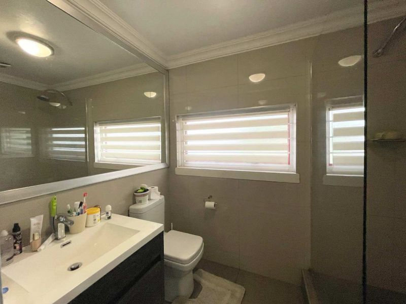 A functional bathroom featuring a modern vanity with integrated basin, large wall mirror, glass-enclosed shower, and neutral tiled finishes throughout.