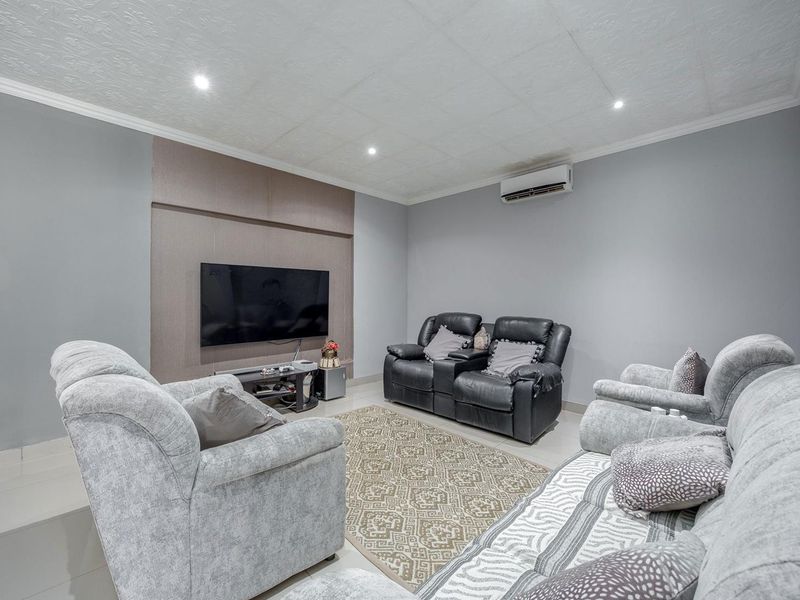 A well-maintained living room featuring tiled flooring, a modern feature wall, recessed downlighting, and a wall-mounted split-system air conditioning unit.