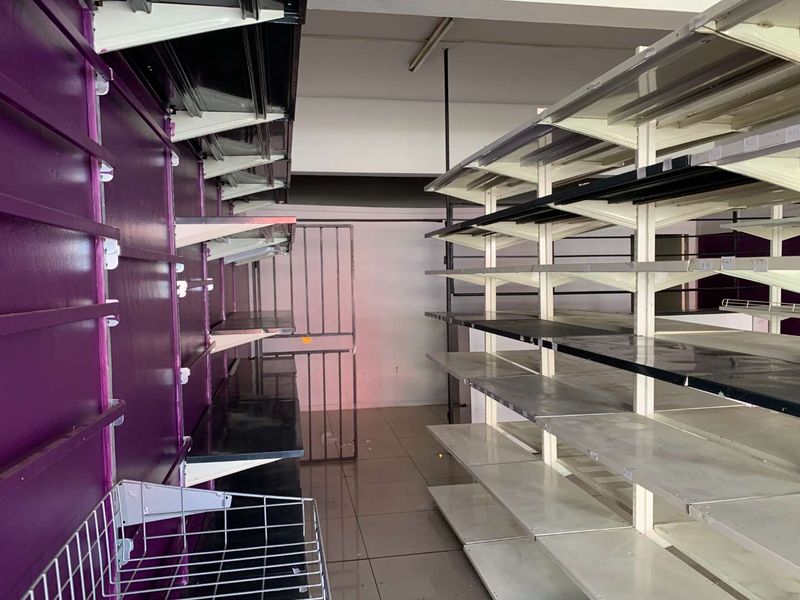 A vacant retail space featuring built-in metal shelving units, slatwall display panels, tiled flooring, and a security gate.