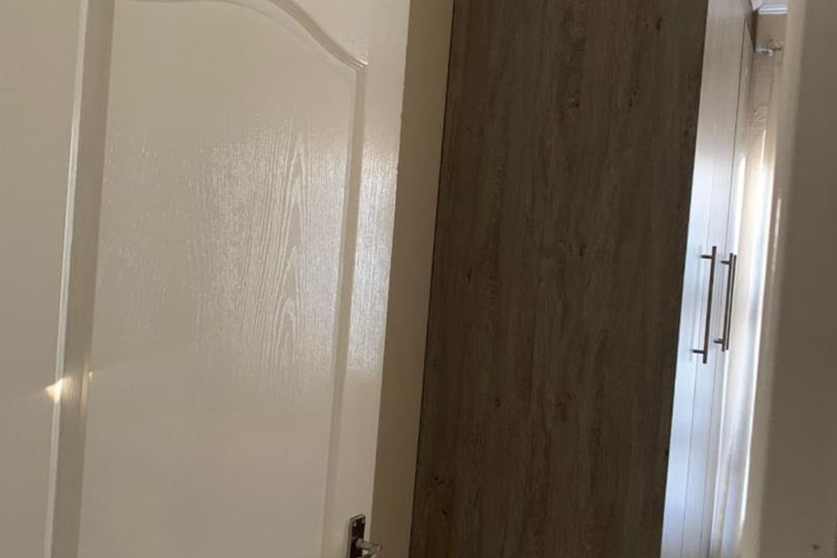 A view of a bedroom interior featuring built-in wooden cabinetry and a white panelled door with modern hardware.