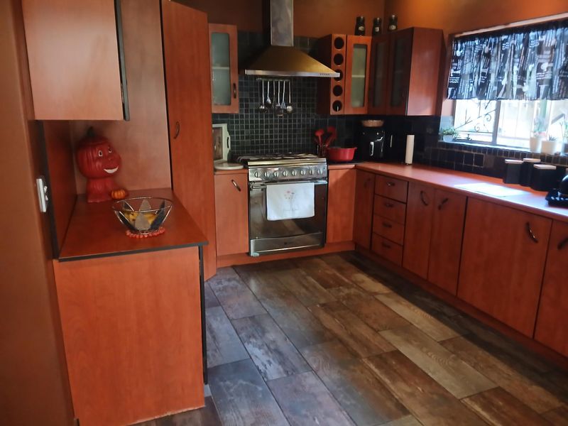 A functional kitchen featuring warm-toned wooden cabinetry, a stainless steel gas stove with extractor fan, tiled backsplash, and wood-look laminate flooring.