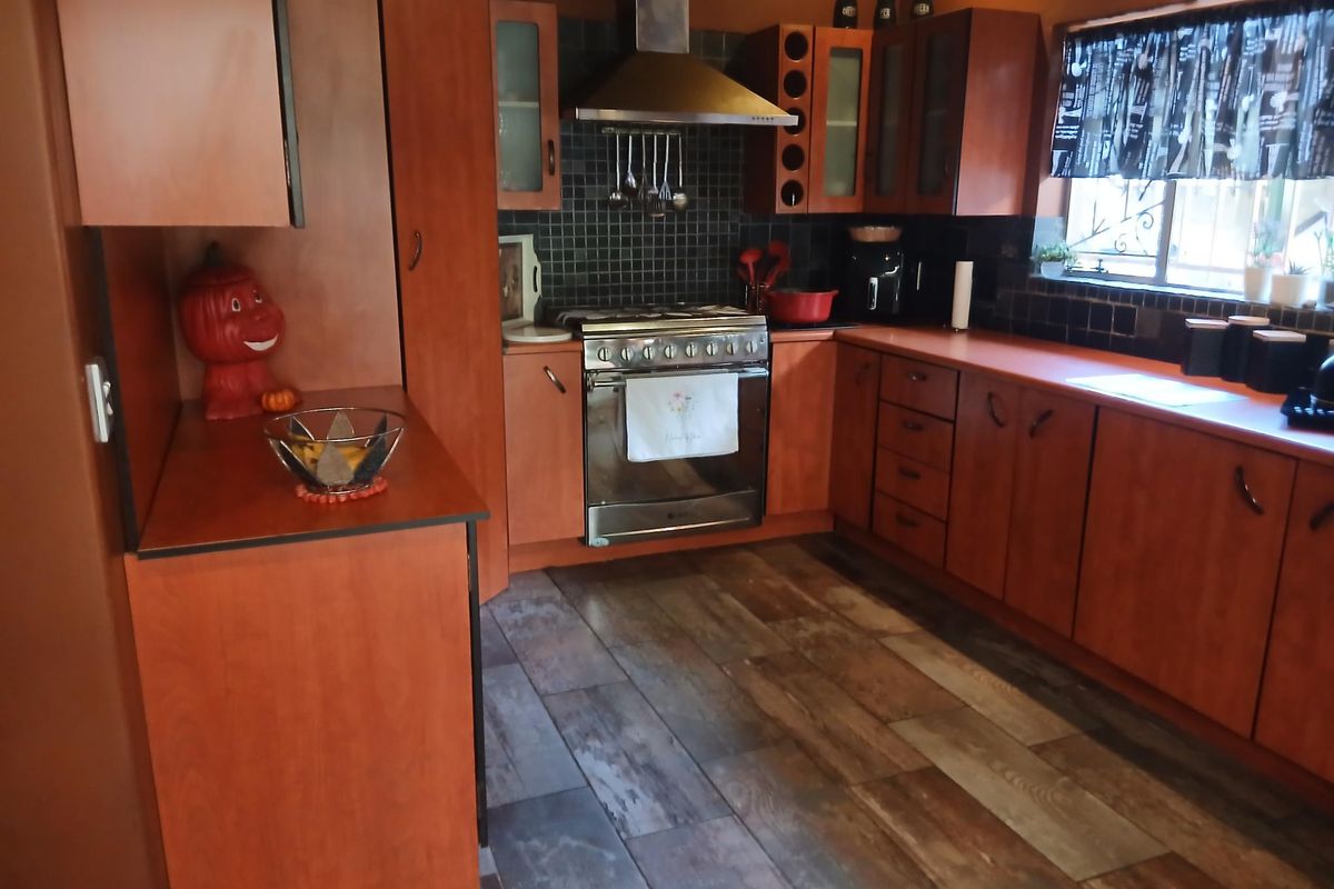 A functional kitchen featuring warm-toned wooden cabinetry, a stainless steel gas stove with extractor fan, tiled backsplash, and wood-look laminate flooring.