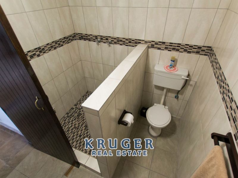 A functional bathroom featuring a tiled walk-in shower area and a standard toilet with neutral wall tiling and decorative mosaic accents.