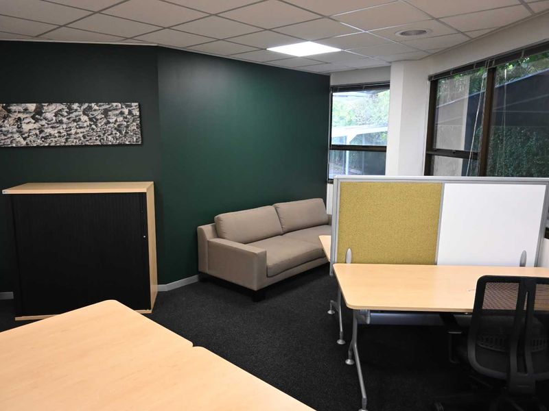 A professional office space featuring a dark accent wall, suspended ceiling with recessed lighting, and large windows providing natural light.