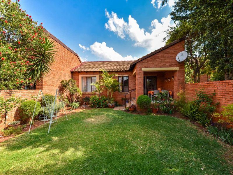 A private rear garden featuring a well-maintained lawn, established landscaping, and a covered patio area attached to the brick townhouse structure.
