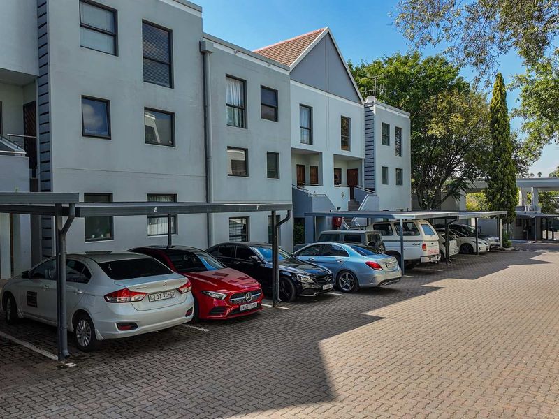 Exterior view of a multi-story apartment complex featuring covered parking bays and a paved driveway area.