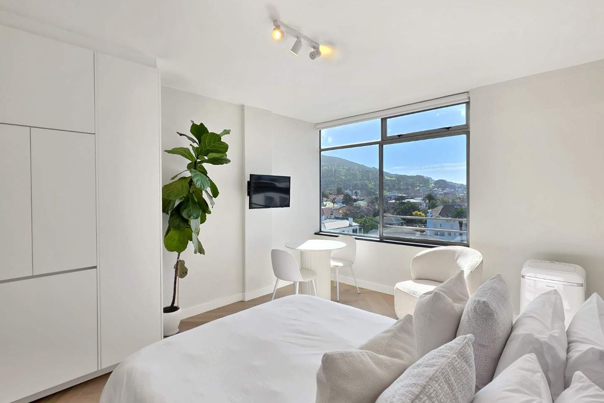 A bright, modern bedroom featuring herringbone flooring, built-in wardrobes, and a large window offering scenic mountain and neighborhood views.