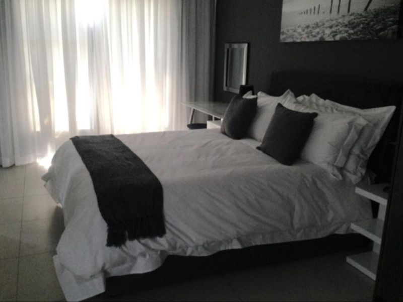 A modern bedroom featuring tiled flooring and floor-to-ceiling sheer curtains, creating a bright and comfortable living space.