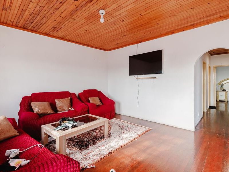 A living room featuring a warm timber tongue and groove ceiling, polished hardwood flooring, and an arched entryway leading to the hallway.